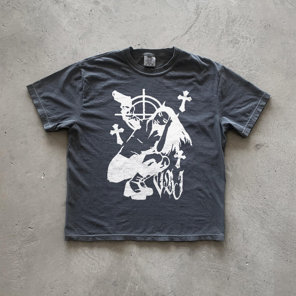 May include: Dark gray t-shirt featuring a graphic design of a stylized female figure holding guns, surrounded by crosses and a target symbol. The style is reminiscent of vintage punk or grunge aesthetics. The graphic is printed in white. The shirt appears to be made of a soft, comfortable fabric.