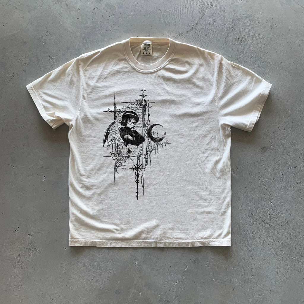 May include: A white t-shirt with a black and white graphic print of an angel with wings, a crescent moon, and a cross. The graphic is surrounded by a black and white design of stylized flowers and leaves.