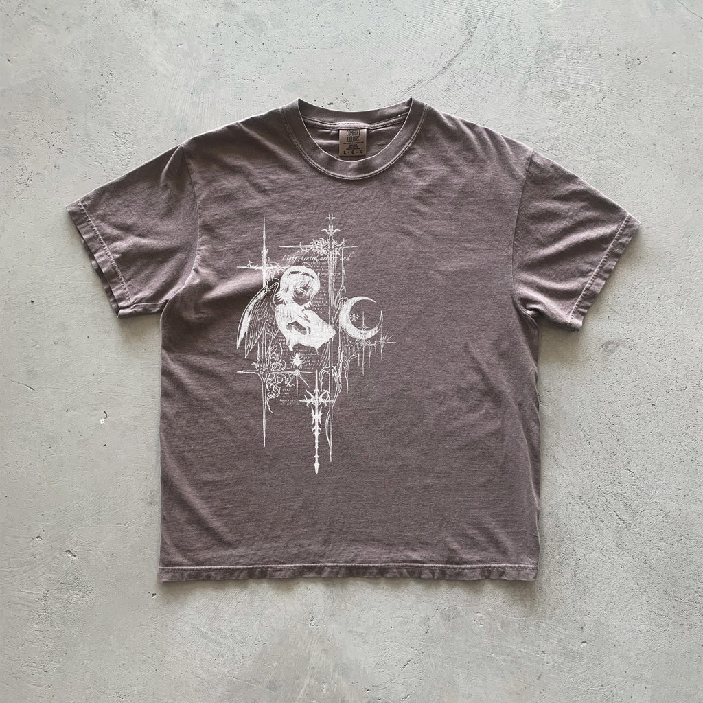 May include: A brown t-shirt with a white graphic print of an angel holding a crescent moon. The graphic is surrounded by a decorative border of lines and crosses.