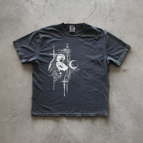 May include: A dark gray t-shirt with a white graphic print of an angel with wings, a crescent moon, and a cross. The graphic is surrounded by a decorative border of lines and crosses. The text 'Lightbringer' is included in the graphic.